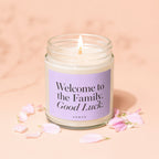 Candle with "Welcome to the Family. Good Luck." text on label, surrounded by petals.
