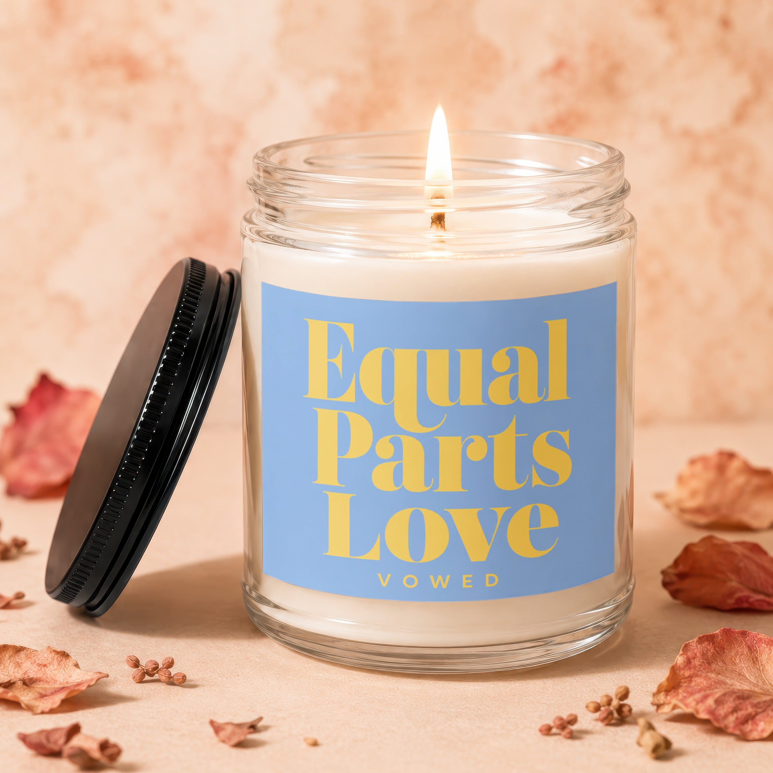Lit candle in glass jar with blue label reading "Equal Parts Love VOWED".