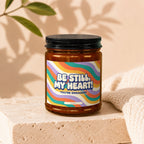 Candle with "Be Still, My Heart! You're Engaged!" text on wavy colorful label.