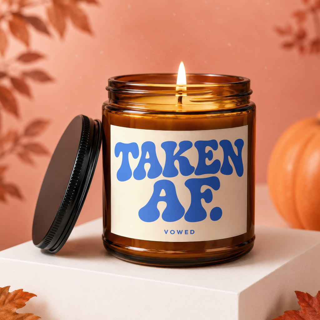 Amber jar candle with lit wick, "TAKEN AF." in blue, and "VOWED" text.