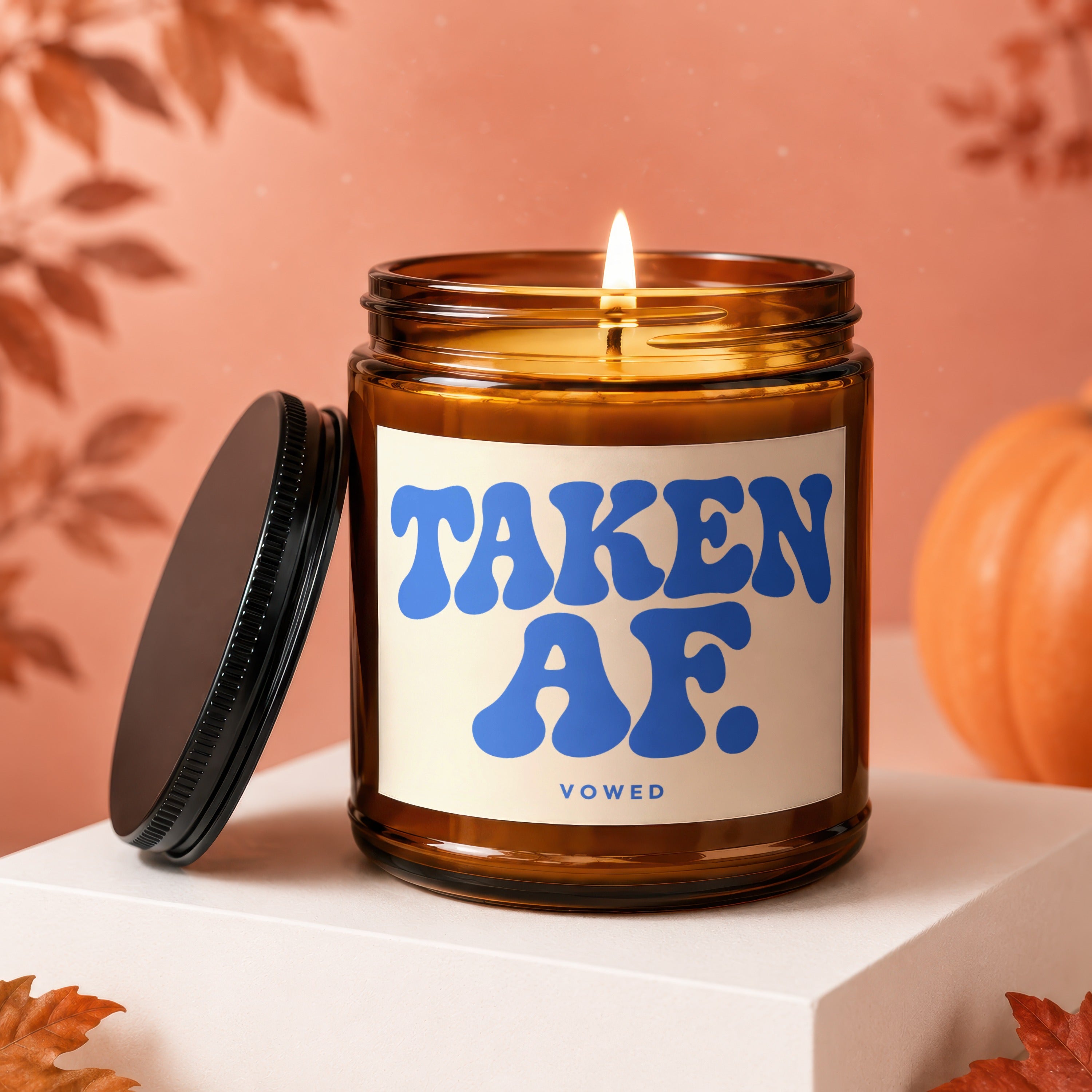 Amber jar candle with lit wick, "TAKEN AF." in blue, and "VOWED" text.