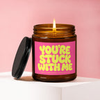 Amber jar candle with pink label reading "YOU'RE STUCK WITH ME" and a lit wick.