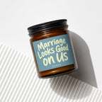 Amber candle in glass jar with black lid, reads "Marriage Looks Good on Us".