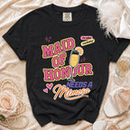 Black t-shirt with "Maid of Honour Needs a Mimosa" text and champagne glass graphic.