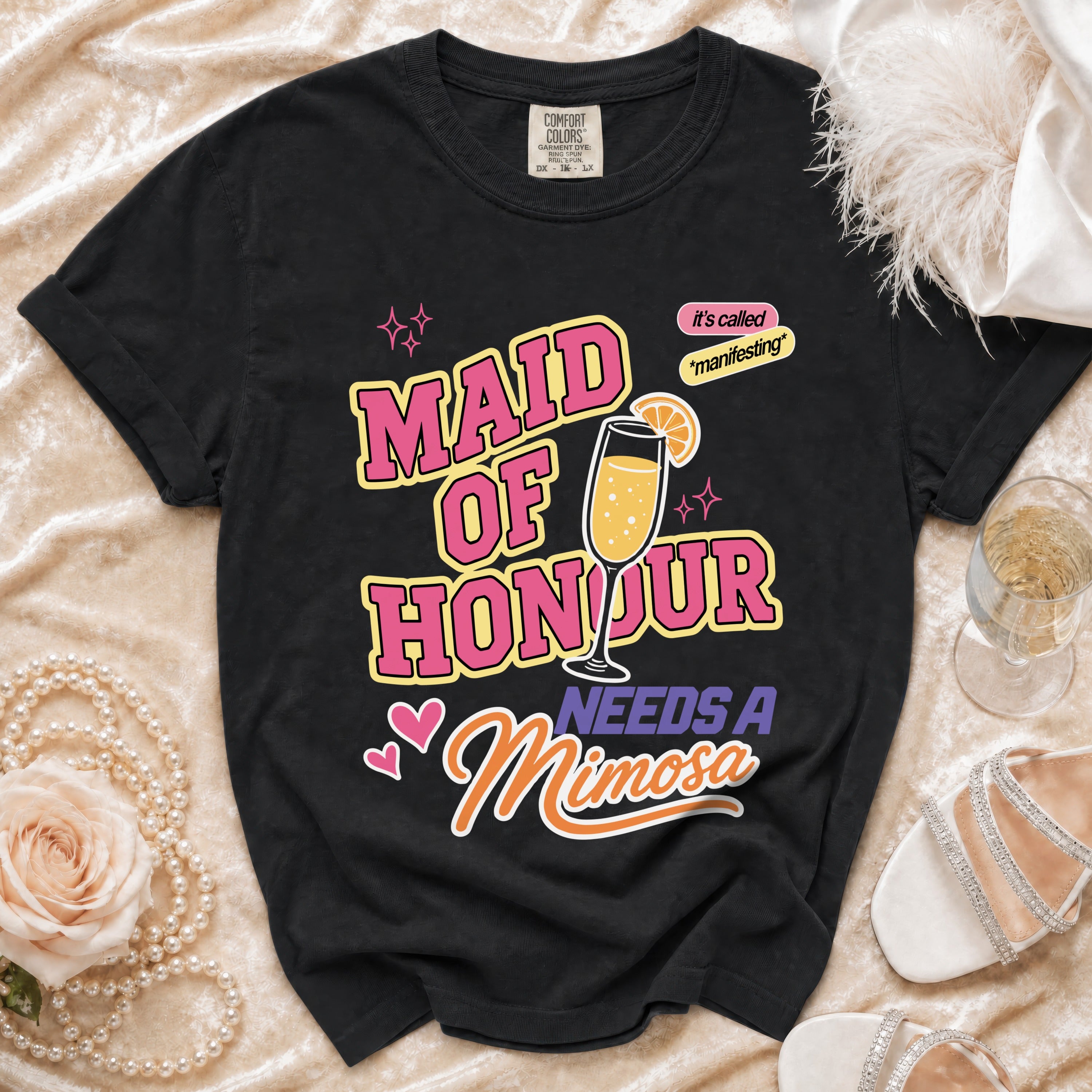 Black t-shirt with "Maid of Honour Needs a Mimosa" text and champagne glass graphic.