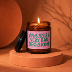 Brown glass candle with lit wick and pink label that reads "Vows, Veils & Very Bad Decisions".
