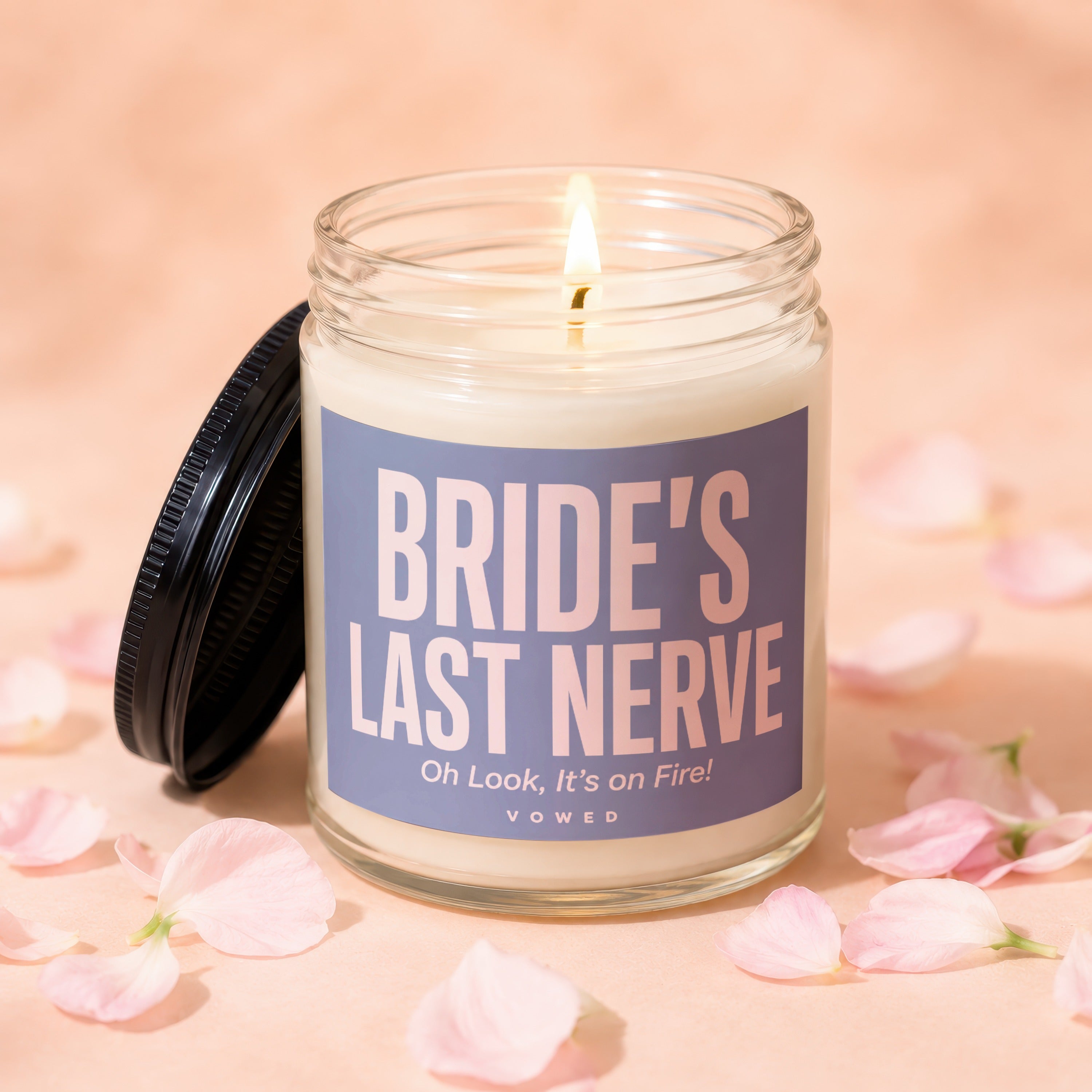 Glass candle with lit wick, reading "BRIDE'S LAST NERVE" and "Oh Look, It's on Fire! VOWED".