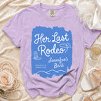 Lavender t-shirt with "Her Last Rodeo Jennifer's Bach" text, cowboy boots, and hat.