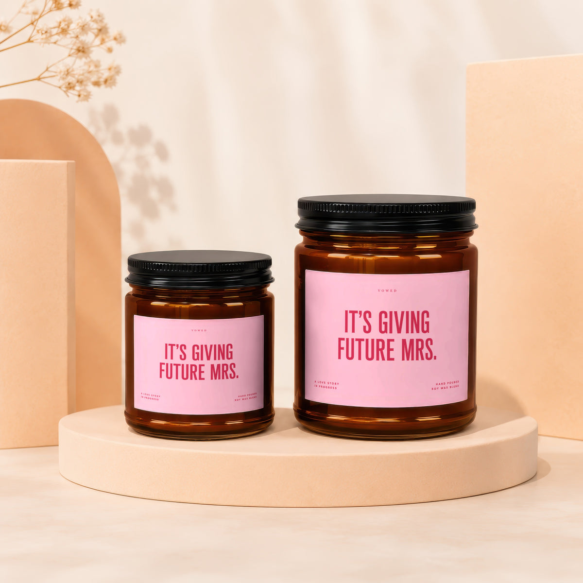Two amber glass candles with pink labels reading "IT'S GIVING FUTURE MRS.".
