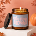 Amber jar candle with lit wick, "Two rings, zero chill" text, and pumpkin decoration.