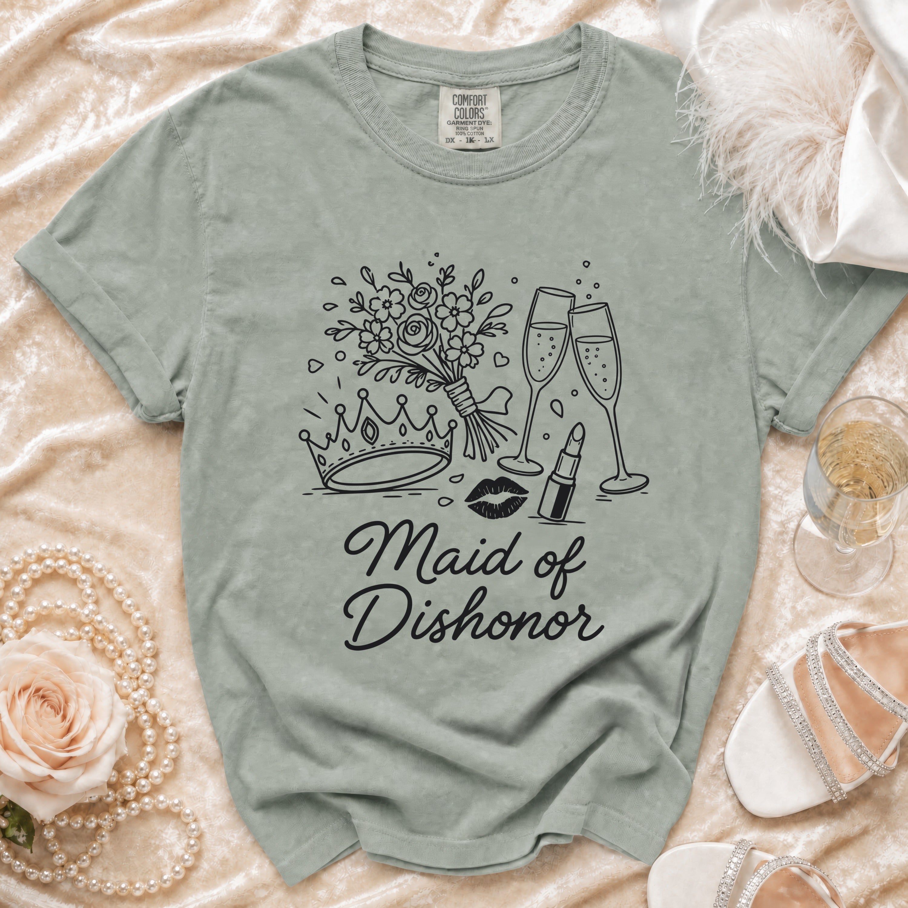 Light green t-shirt with black line art of crown, lips, lipstick, flowers, and champagne glasses with text "Maid of Dishonor".