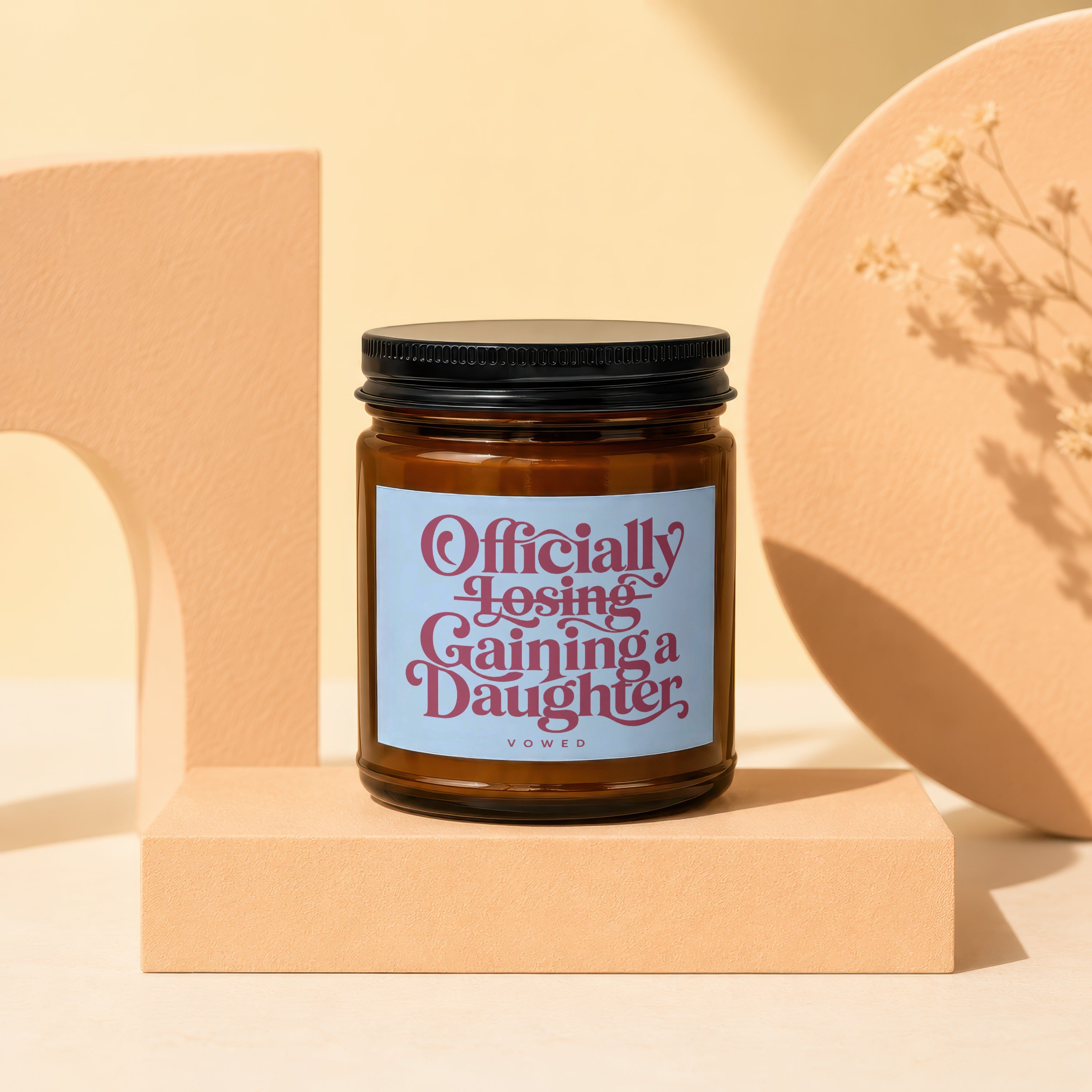Brown glass candle with a blue label reading "Officially Losing Gaining a Daughter".