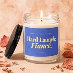 Glass candle with lit flame, blue label reading "Hard Launch: Fiancé."