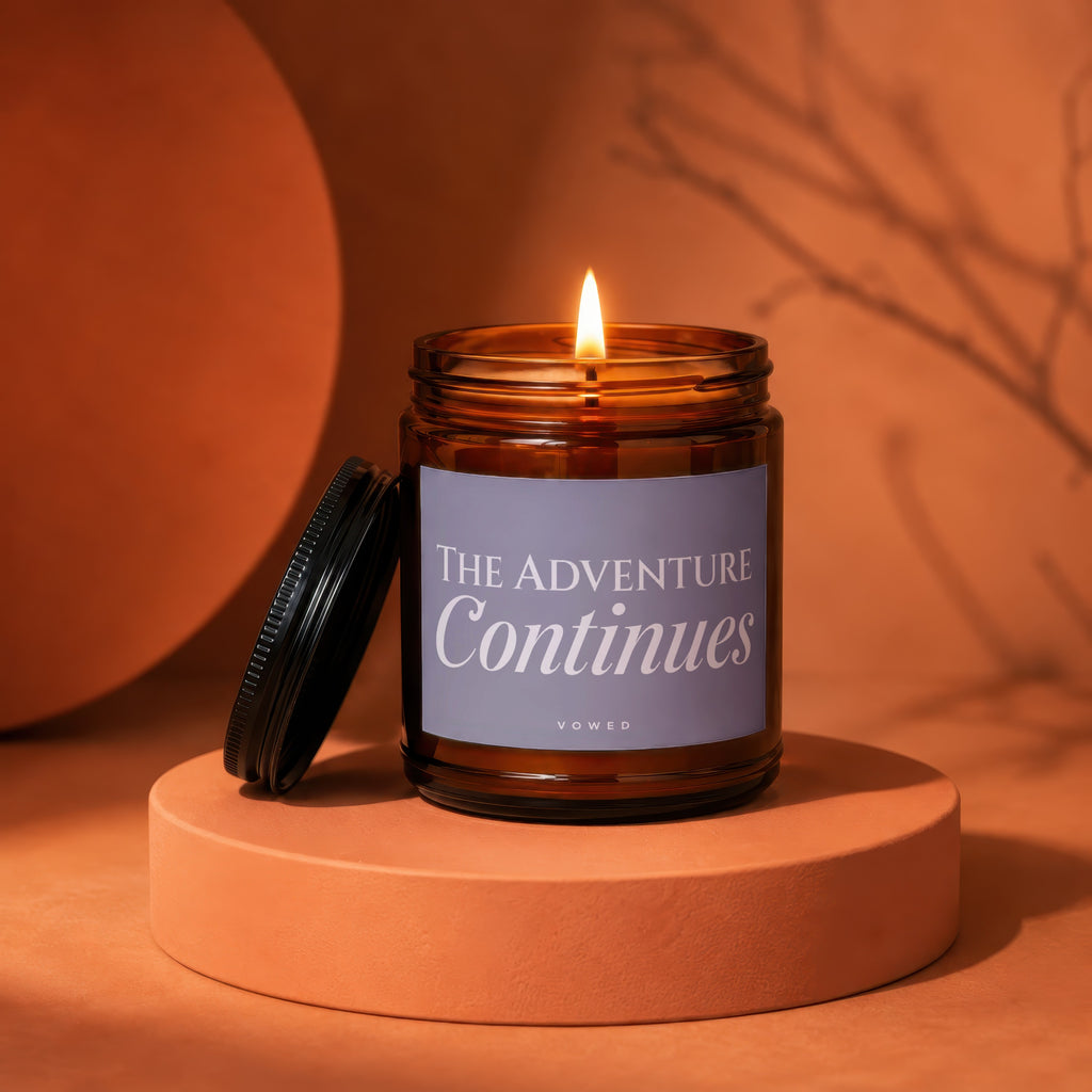 Burning amber glass candle with lid off, labeled "THE ADVENTURE Continues".