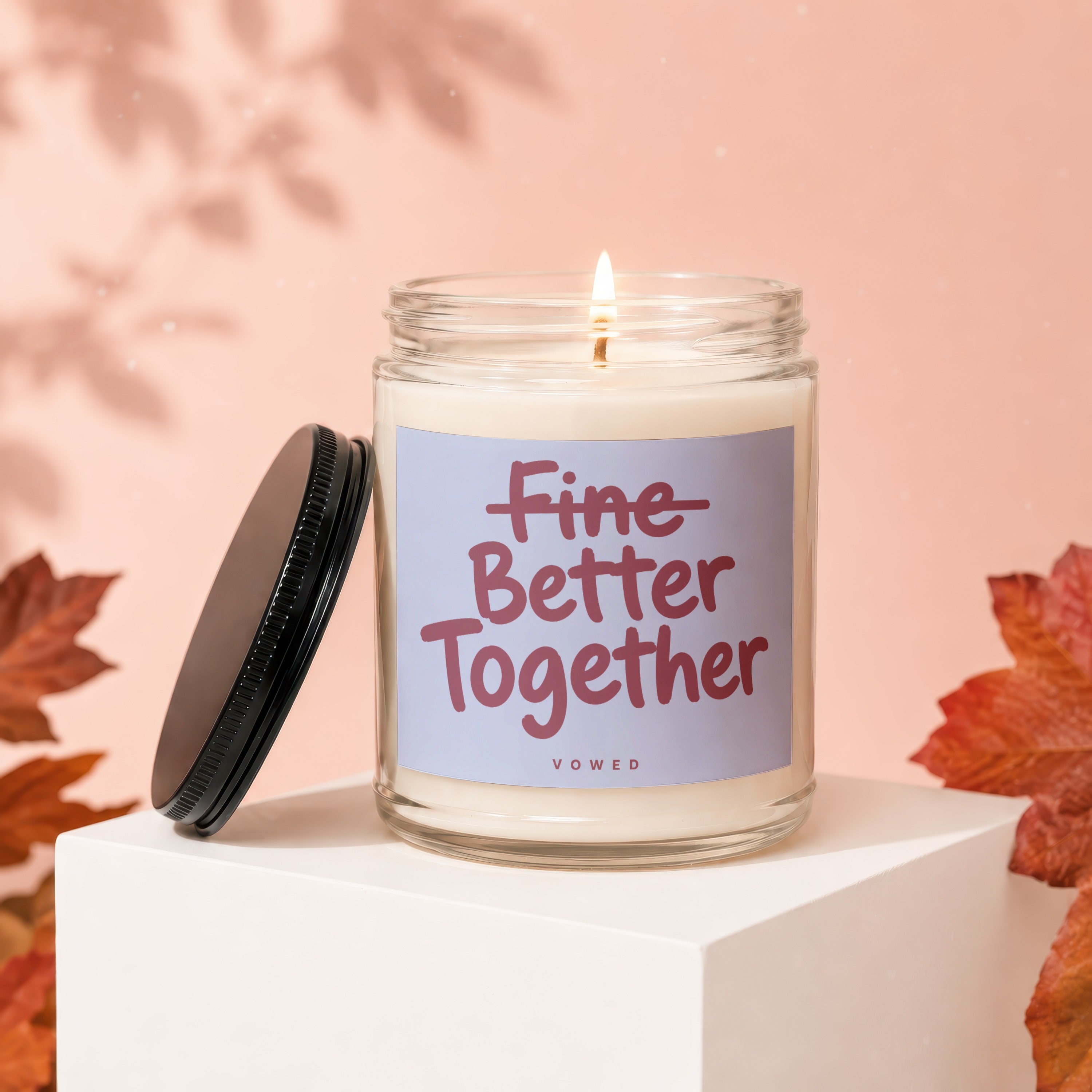 Candle with "Fine Better Together" text and a lit wick, with autumn leaves.