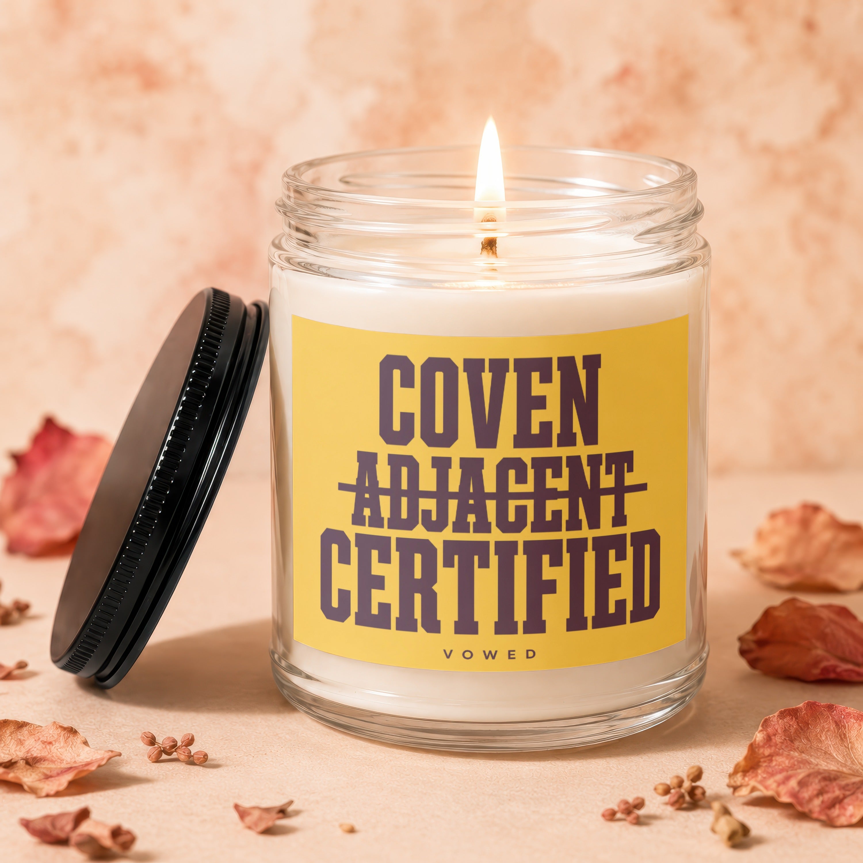 Candle with yellow label reading "Coven Adjacent Certified" and "Vowed".