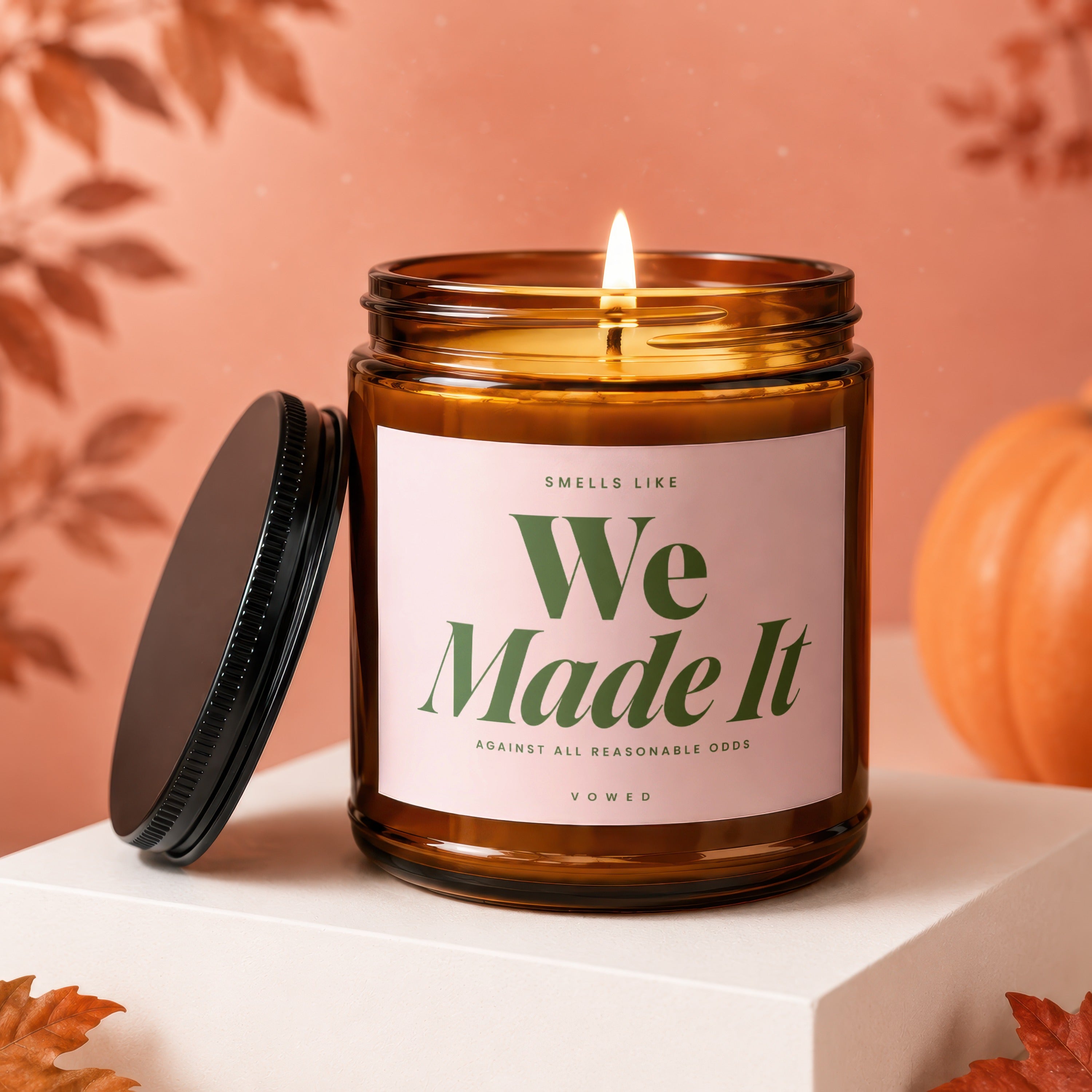 Brown glass candle with lit flame and pink label that reads "We Made It"
