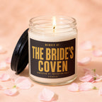 Scented candle with label "Member of: The Bride's Coven" surrounded by pink petals.