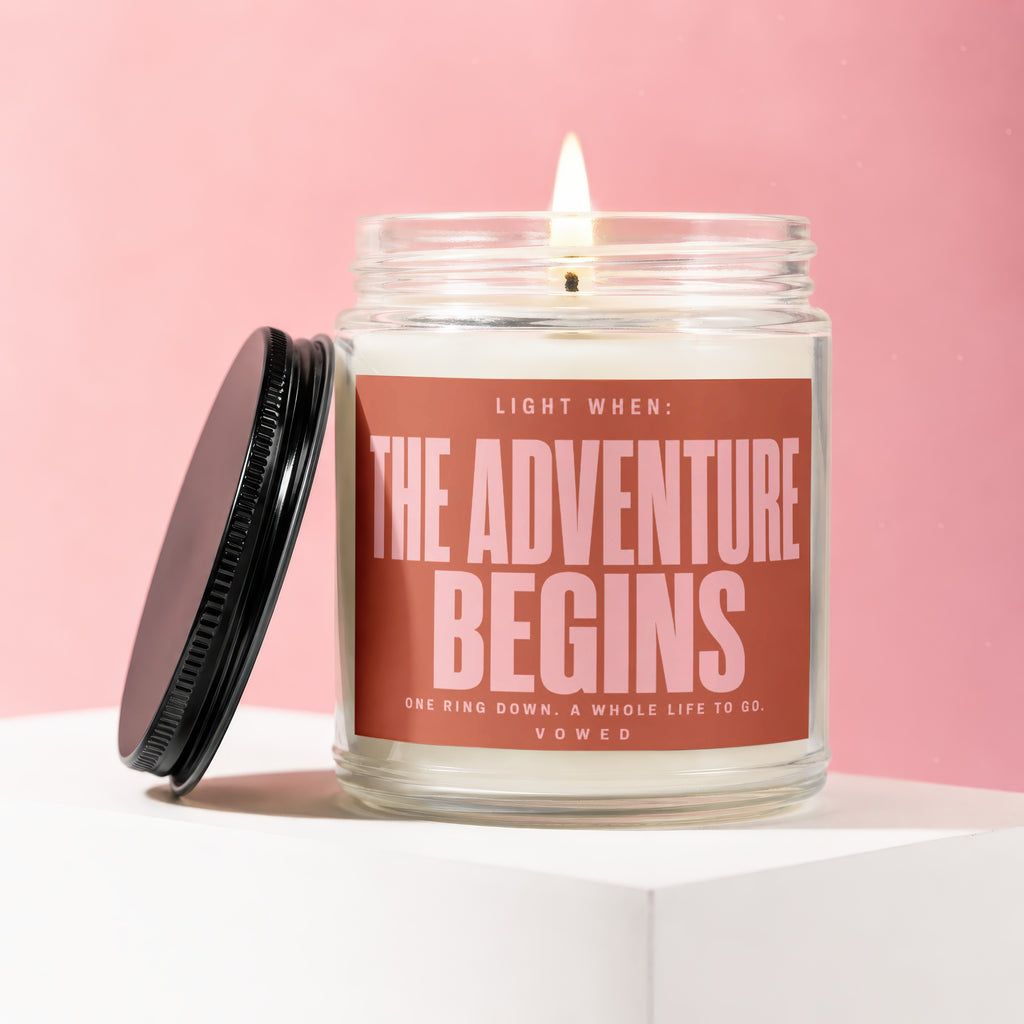 Candle with "The Adventure Begins" text on a pink background