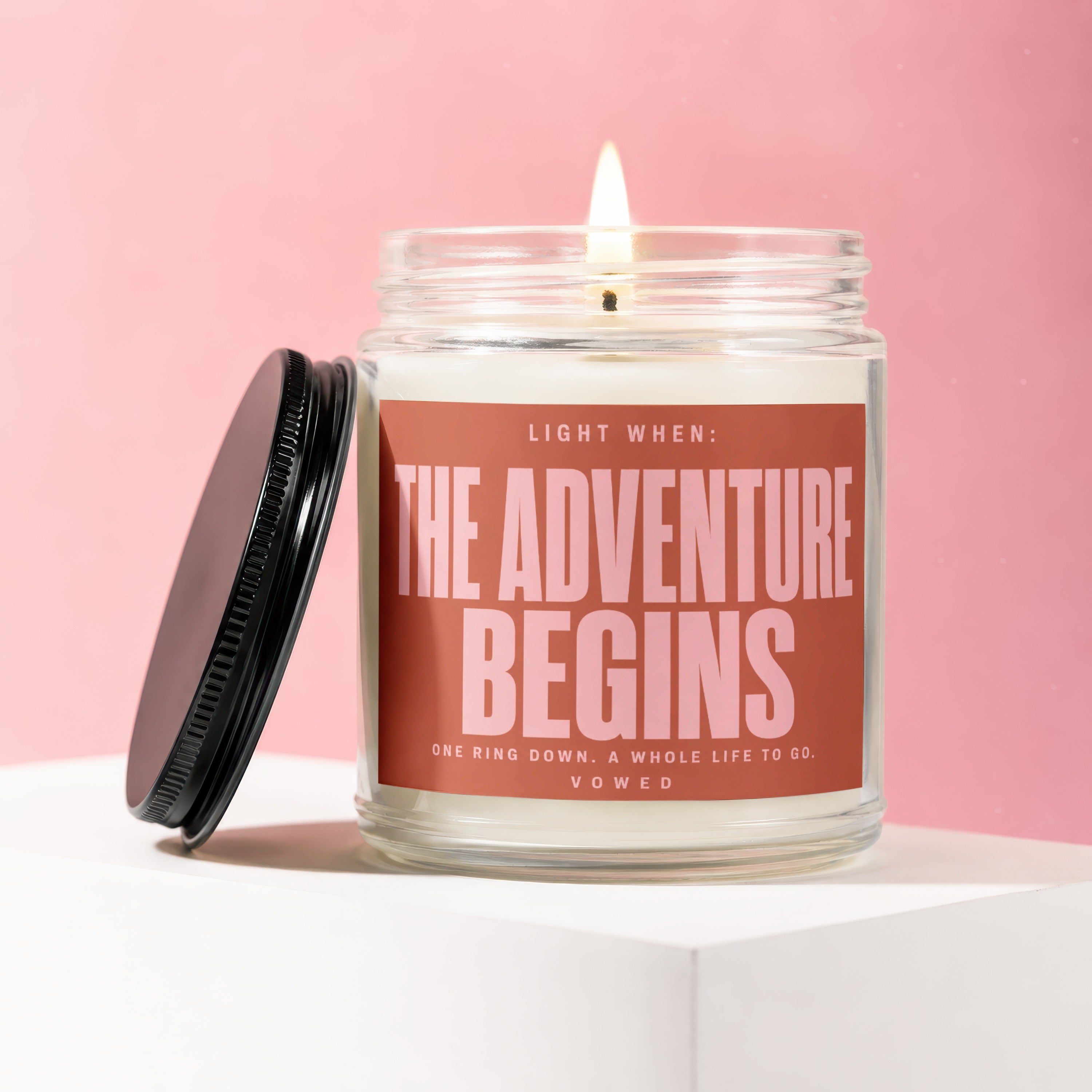 Candle with "The Adventure Begins" text on a pink background
