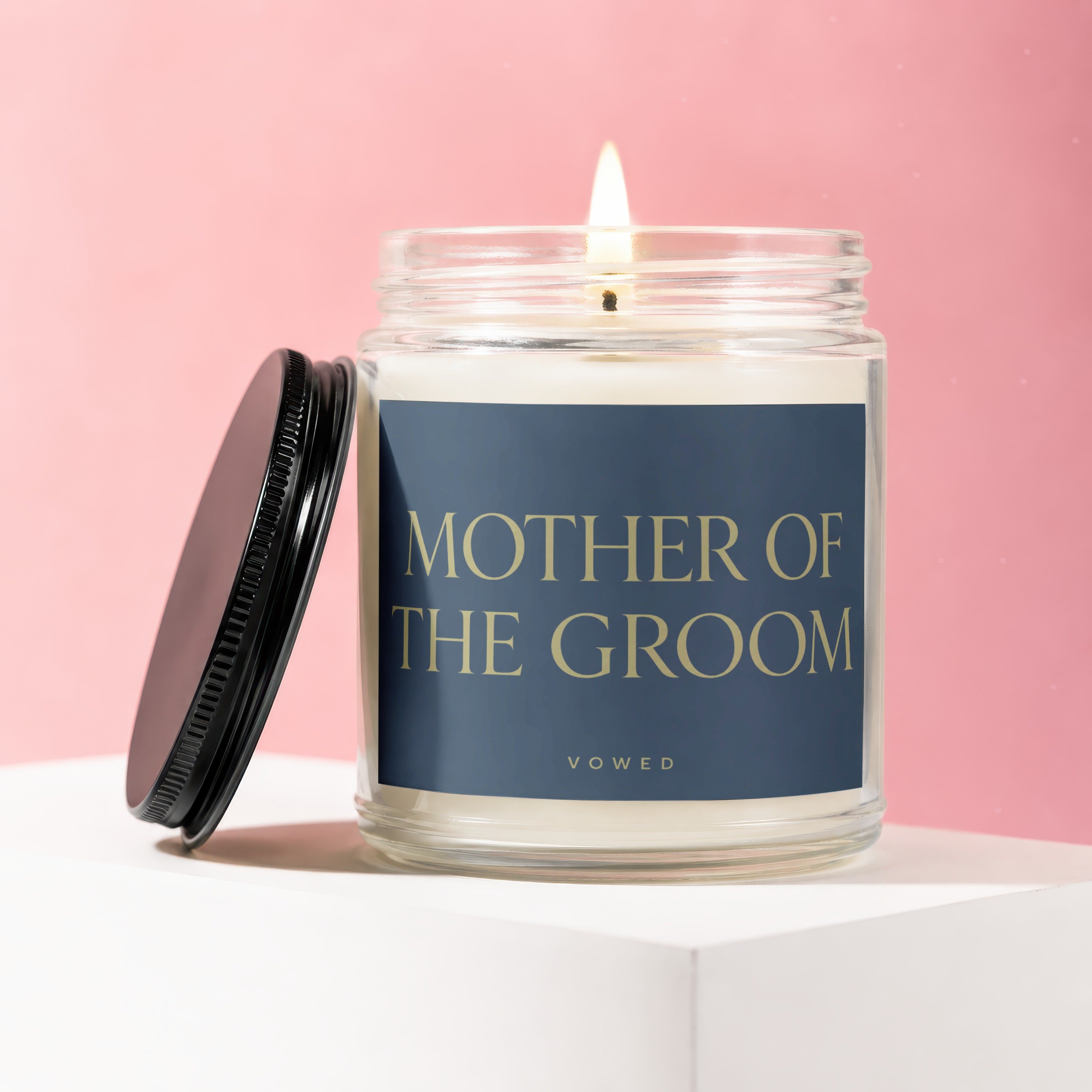 Glass candle with lit wick and dark lid, reads "MOTHER OF THE GROOM".