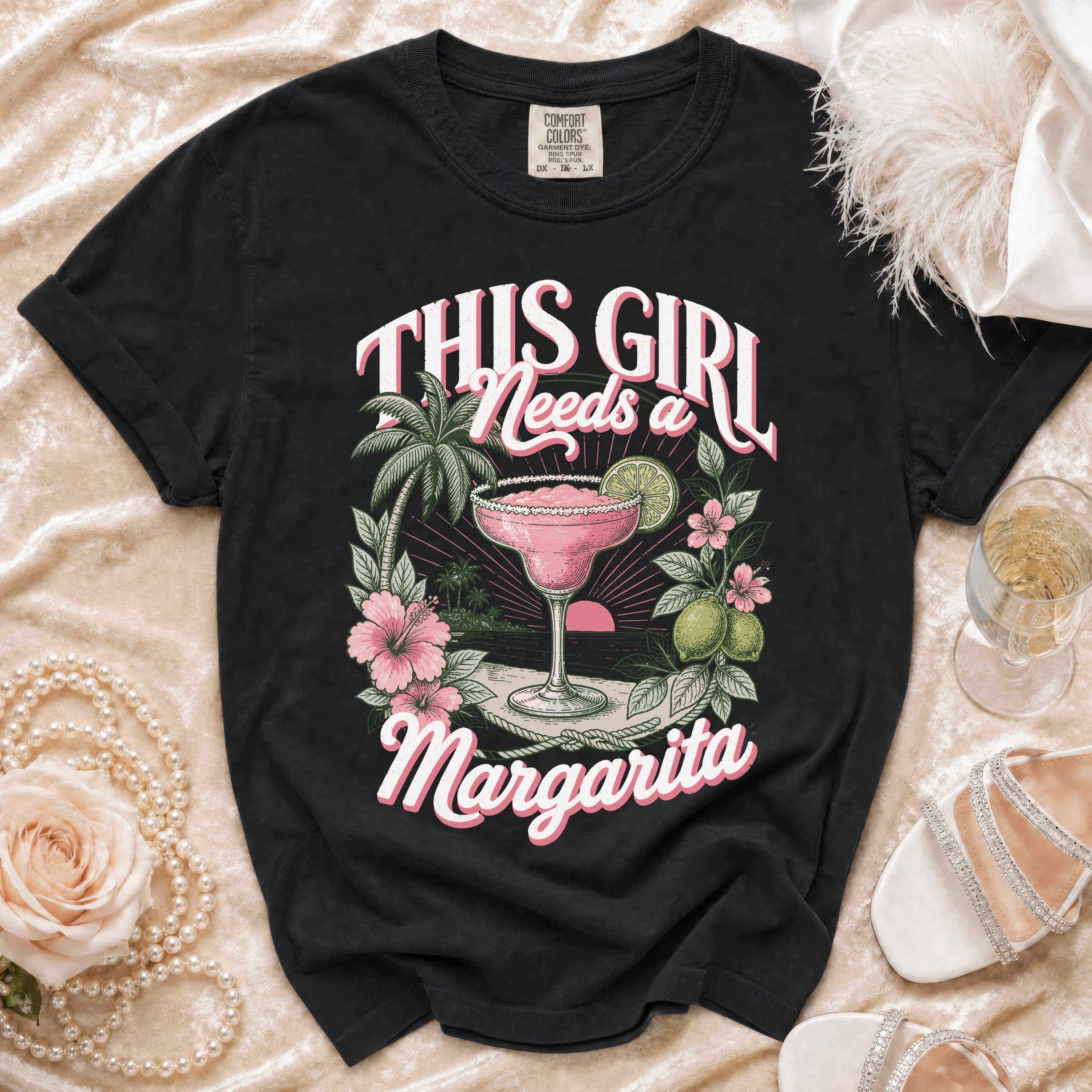 Black t-shirt with "This Girl Needs a Margarita" text and a tropical cocktail graphic.
