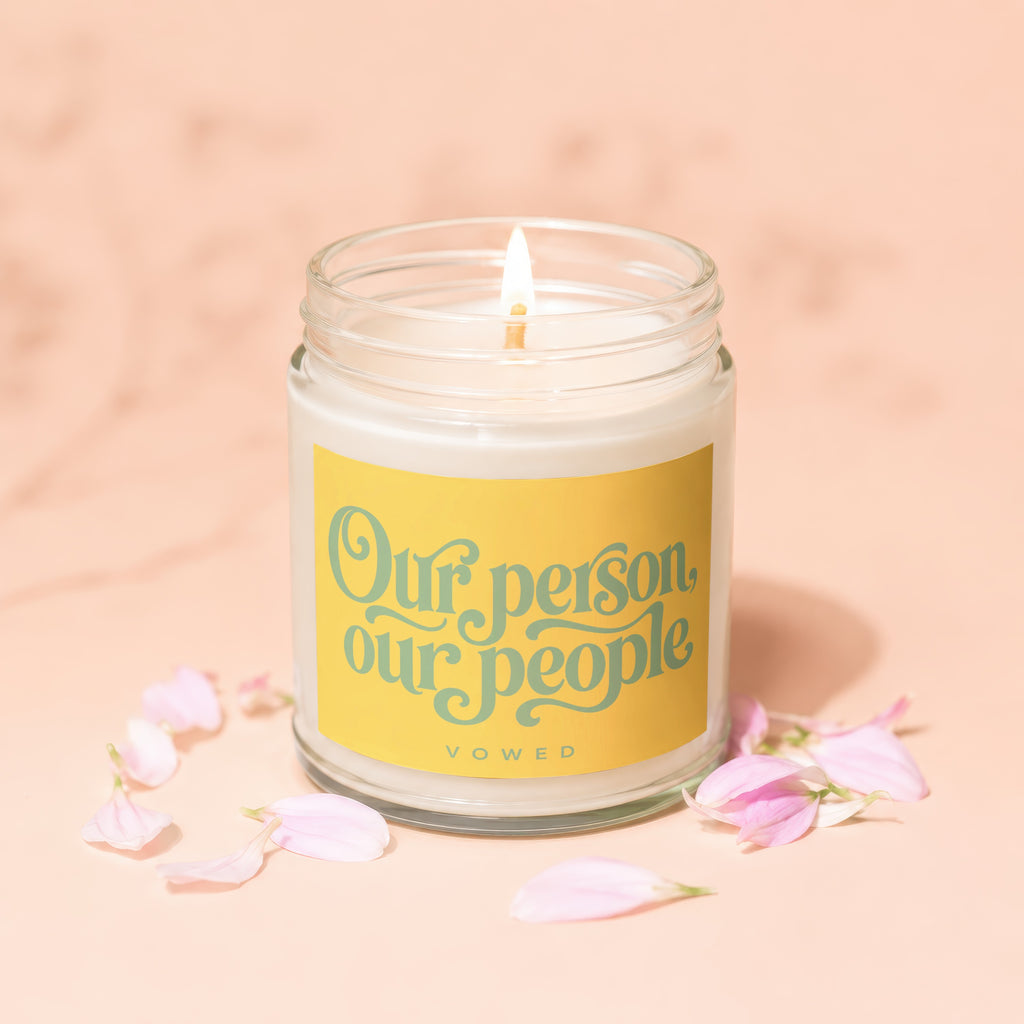 Candle with yellow label reading "Our person, our people" surrounded by pink petals.