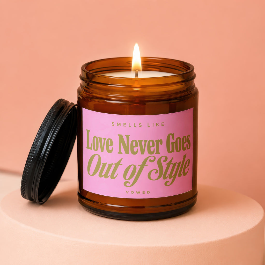 Brown glass candle with pink label that reads "Smells Like Love Never Goes Out of Style".
