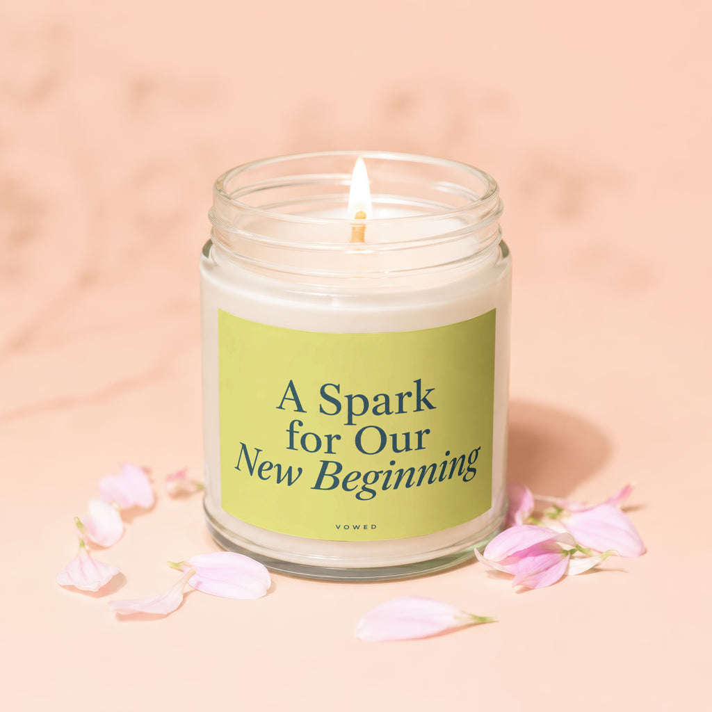 Glass jar candle with lit flame and "A Spark for Our New Beginning" text.