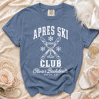Blue crewneck t-shirt featuring white retro text reading "APRES SKI CLUB OLIVIA'S BACHELORETTE ASPEN CO" with crossed skis, a martini glass, and snowflakes.