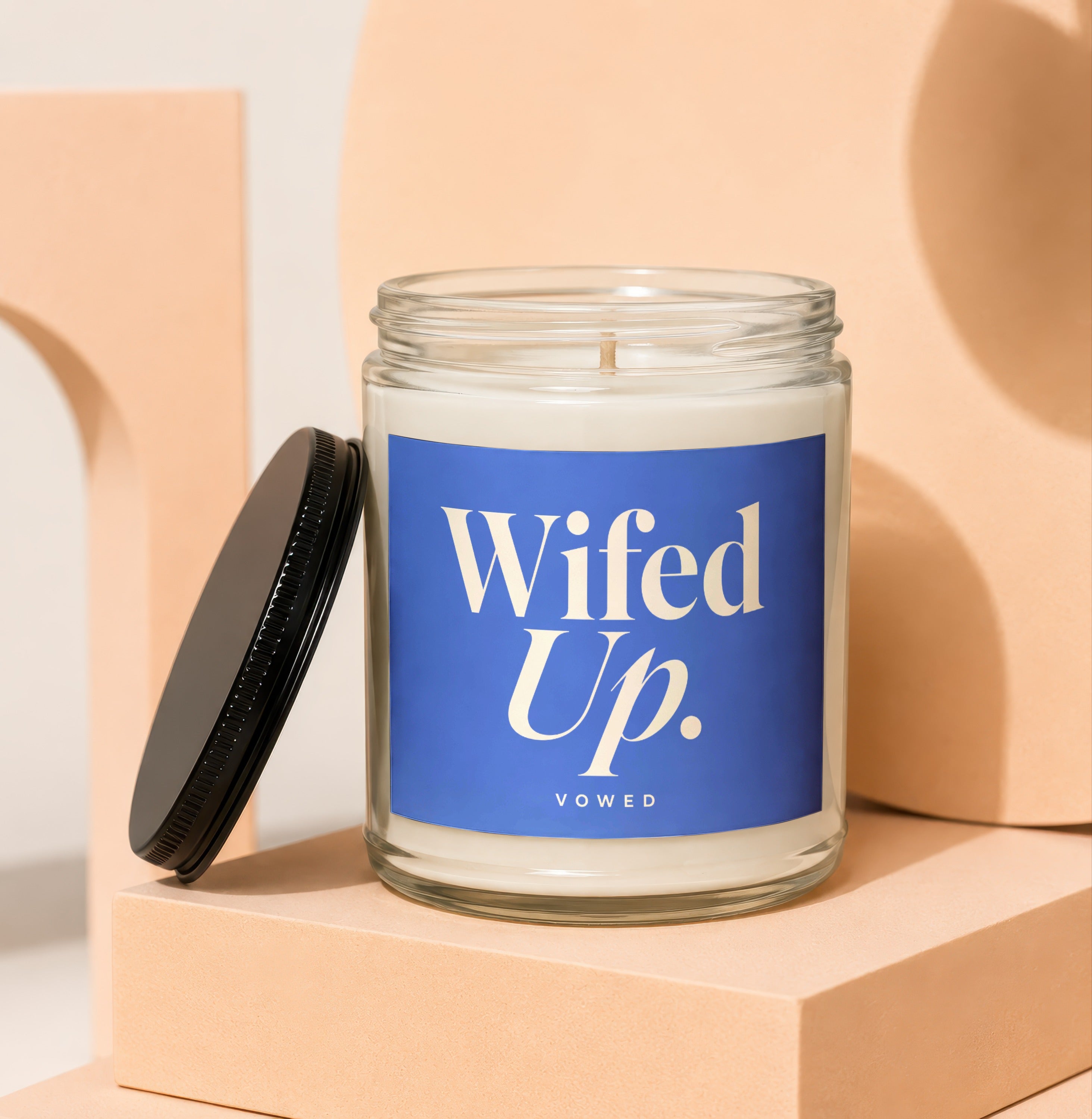 Glass candle with white wax and blue label reading "Wifed Up. VOWED".