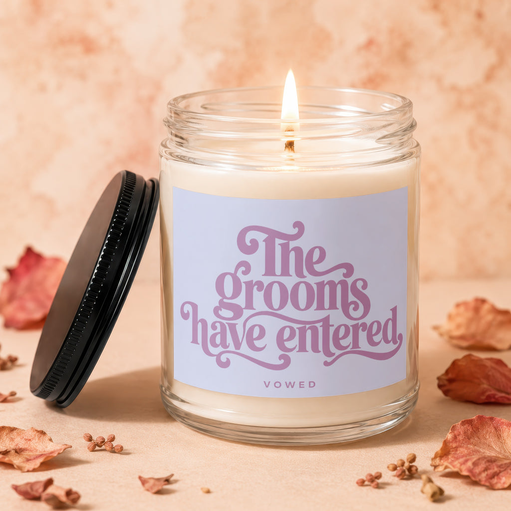 Glass jar candle with lit wick and label reading "The grooms have entered VOWED."