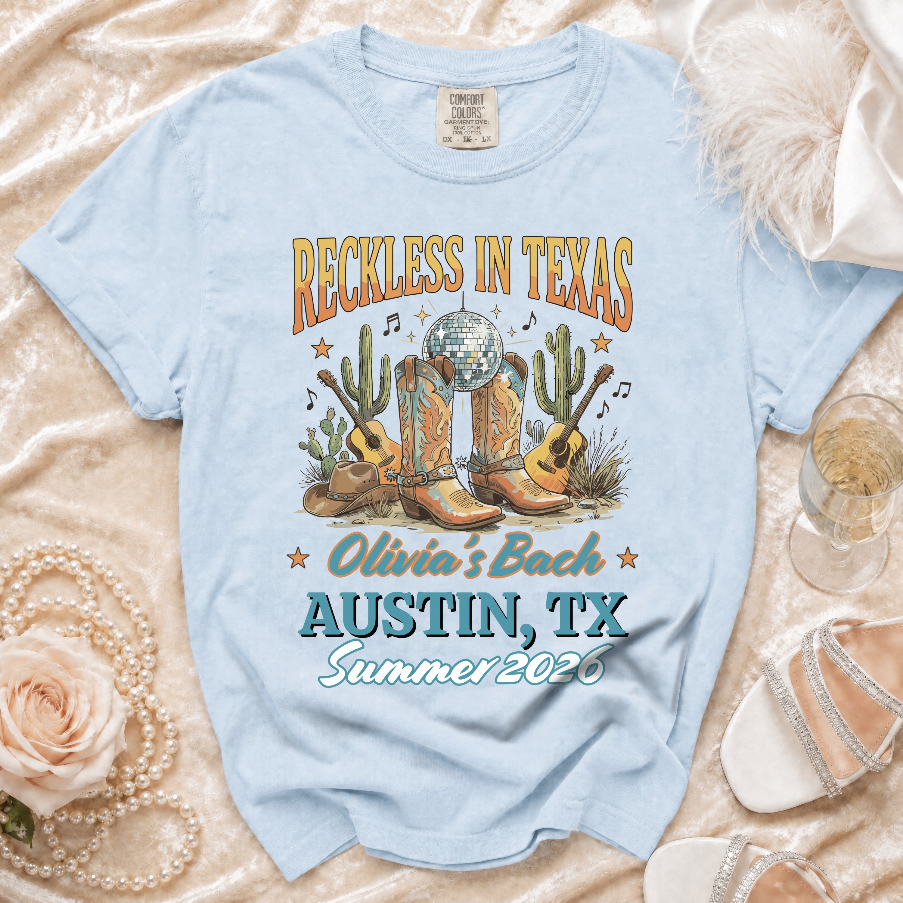 Light blue t-shirt with "Reckless in Texas Olivia's Bach Austin, TX Summer 2026" text.