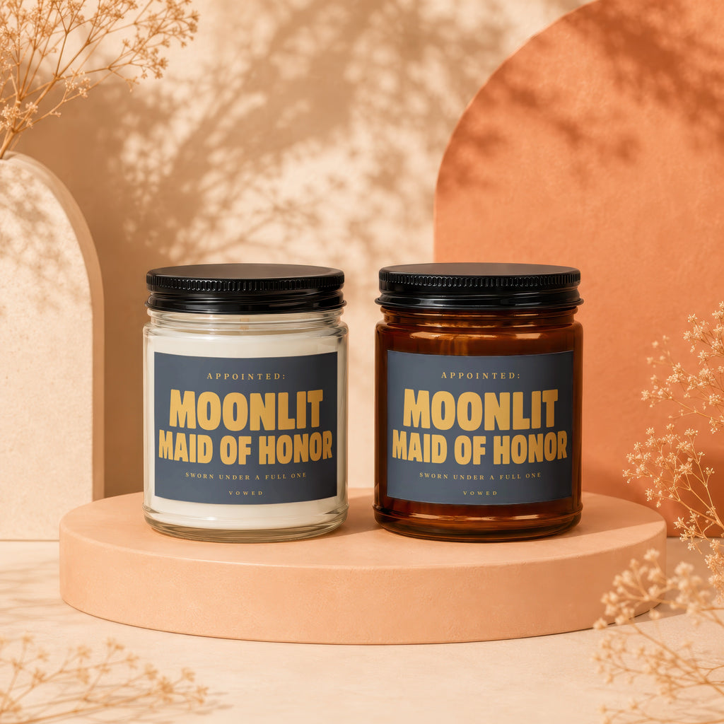 Two candles, one clear and one amber, labeled "Moonlit Maid of Honor" with black lids.