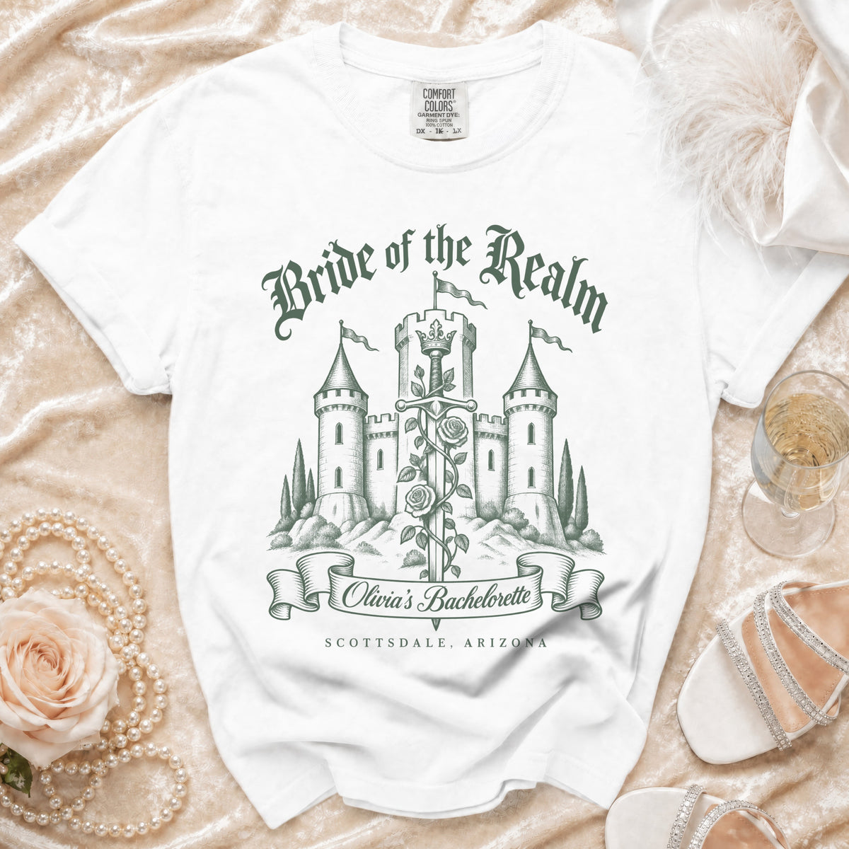 White t-shirt with a green graphic featuring a castle, a sword, roses, and bachelorette text.