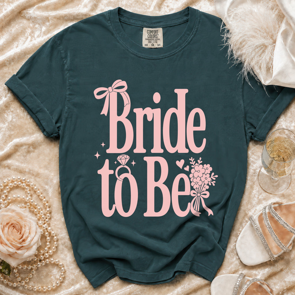 Dark teal t-shirt with pink "Bride to Be" text, ring, bow, and flowers.