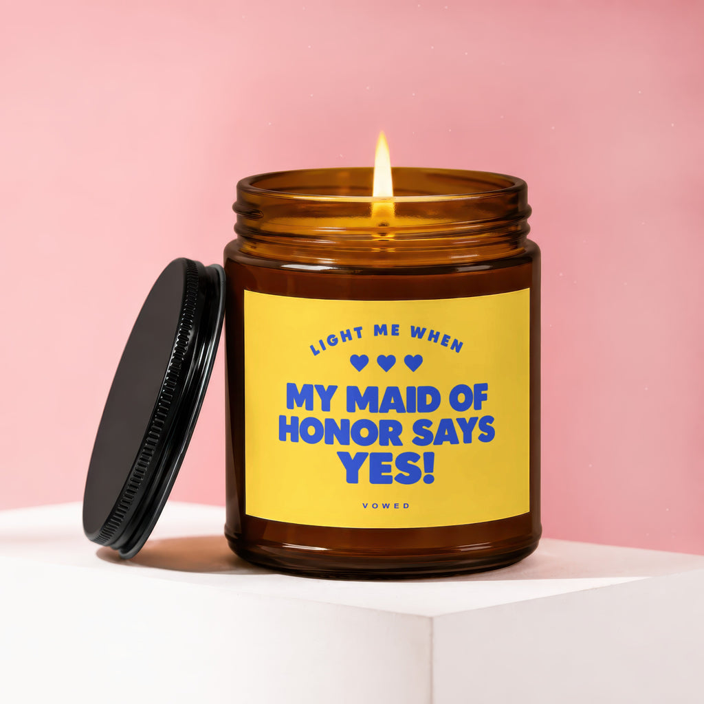 Amber candle with burning wick and black lid, reads "Light me when my maid of honor says yes!"