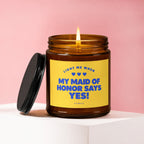 Amber candle with burning wick and black lid, reads "Light me when my maid of honor says yes!"