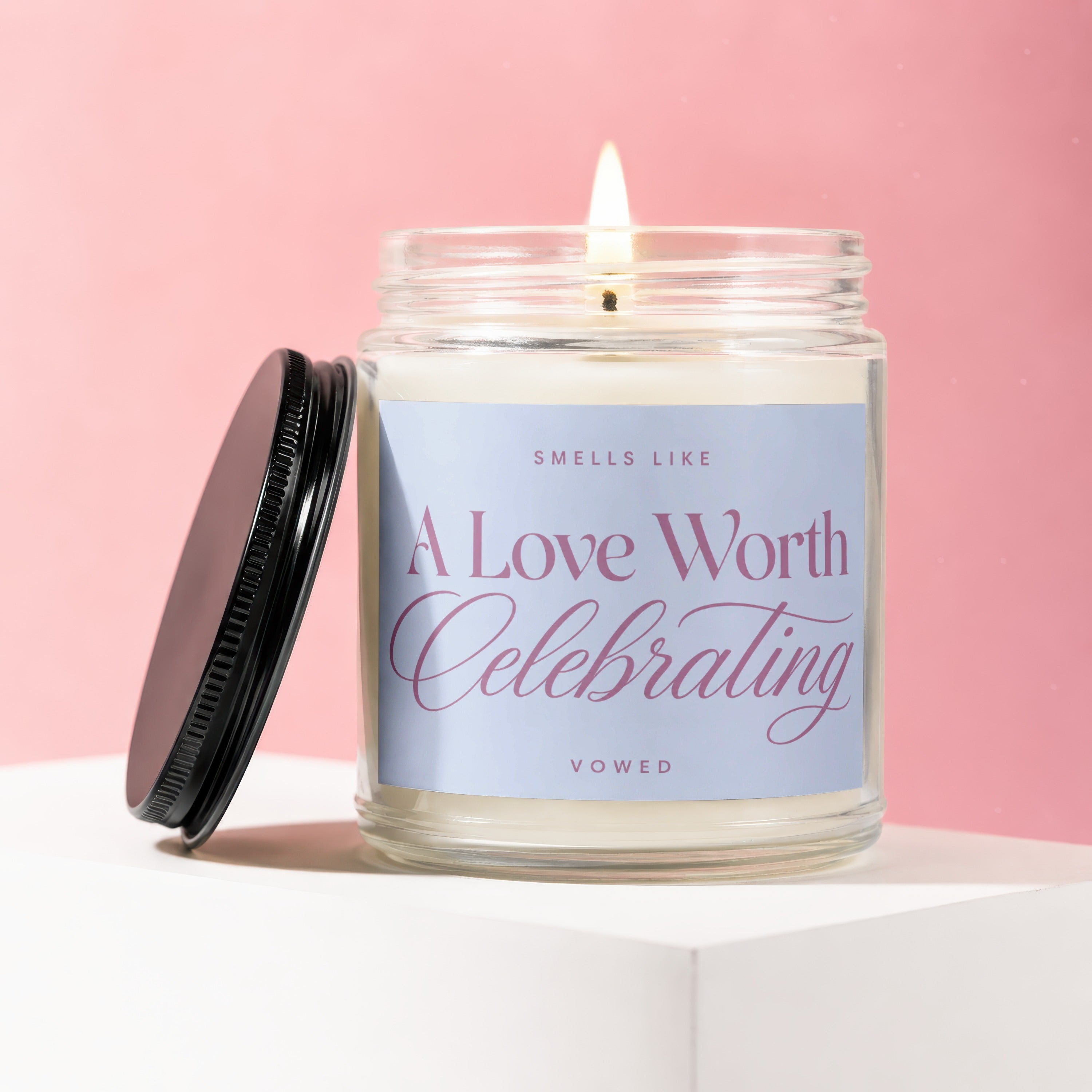 Lit candle in glass jar with black lid, text "Sells Like A Love Worth Celebrating VOWED".