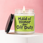 Glass candle labeled "Maid of Honor On Off Duty" with black lid on pink background.