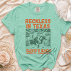 Green t-shirt with "Reckless in Texas" and "Olivia's Bach" text, bull rider graphic.