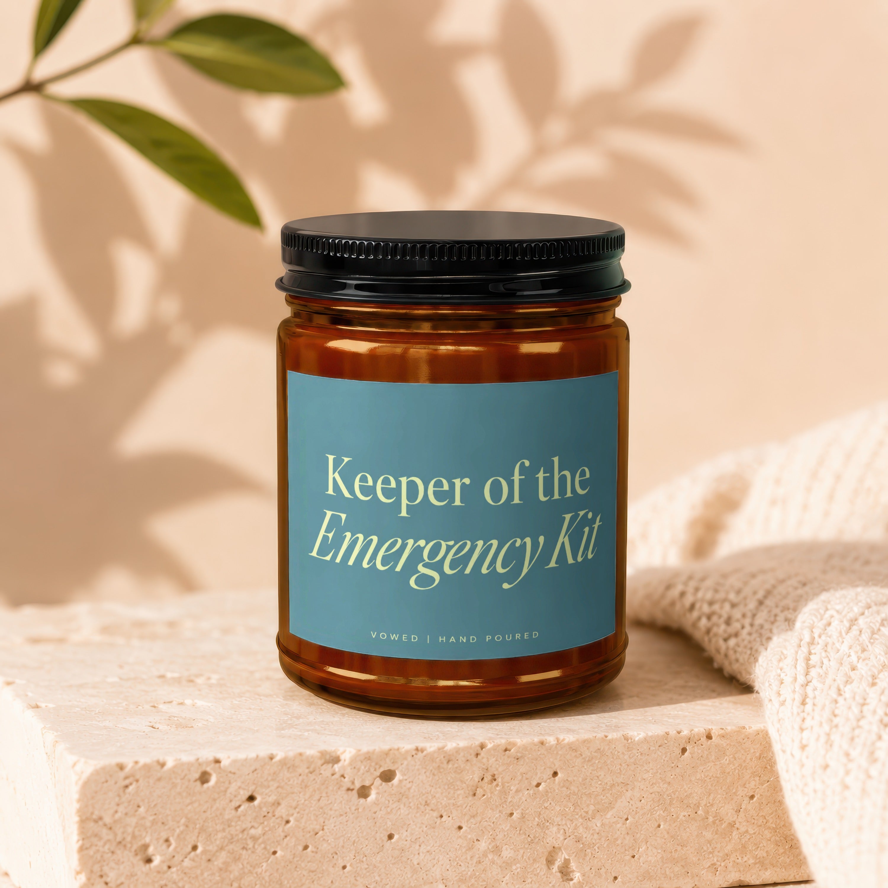 Amber glass candle labeled "Keeper of the Emergency Kit" with "Vowed | Hand Poured".