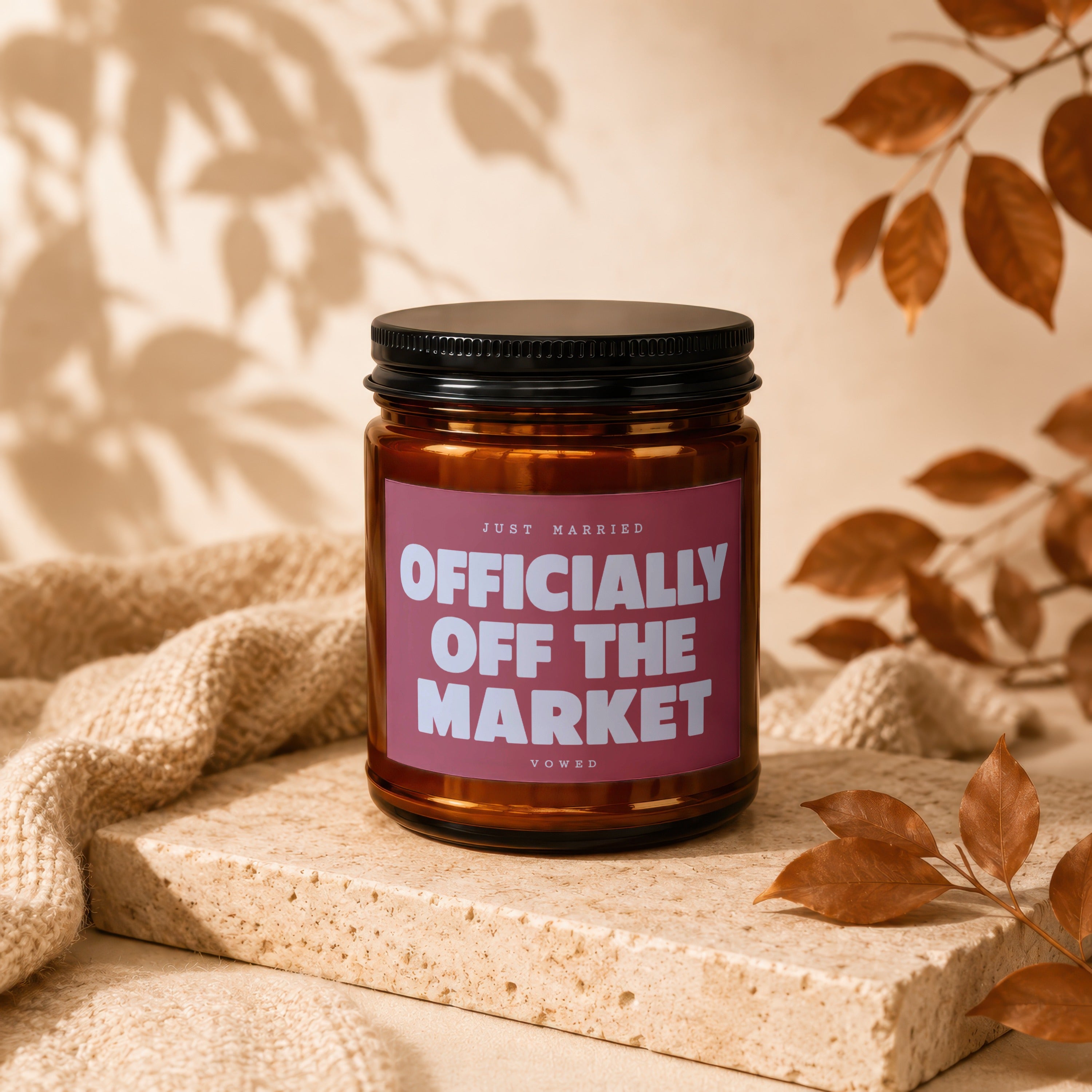 Amber jar candle with "Officially Off The Market" text, with cozy textured blanket and autumn leaves.