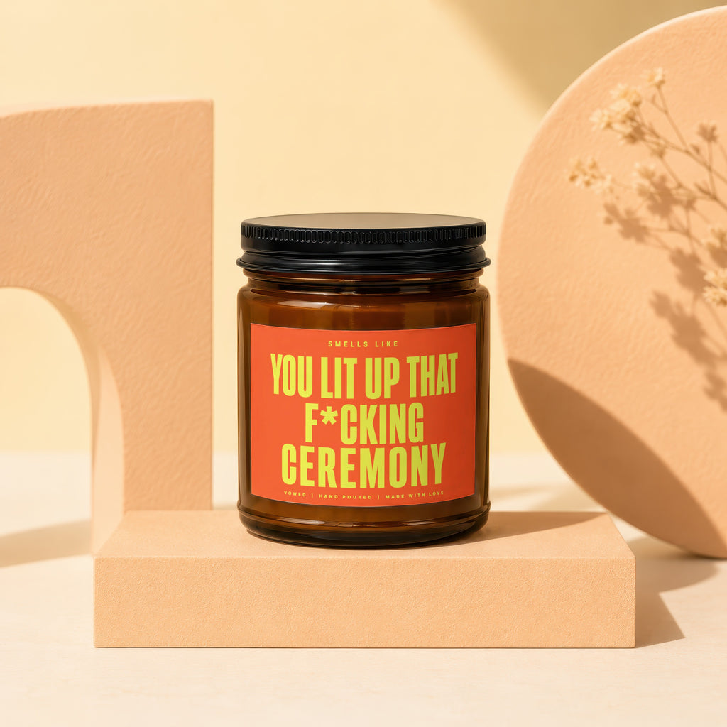 Brown jar candle with orange label reading "YOU LIT UP THAT F*CKING CEREMONY".