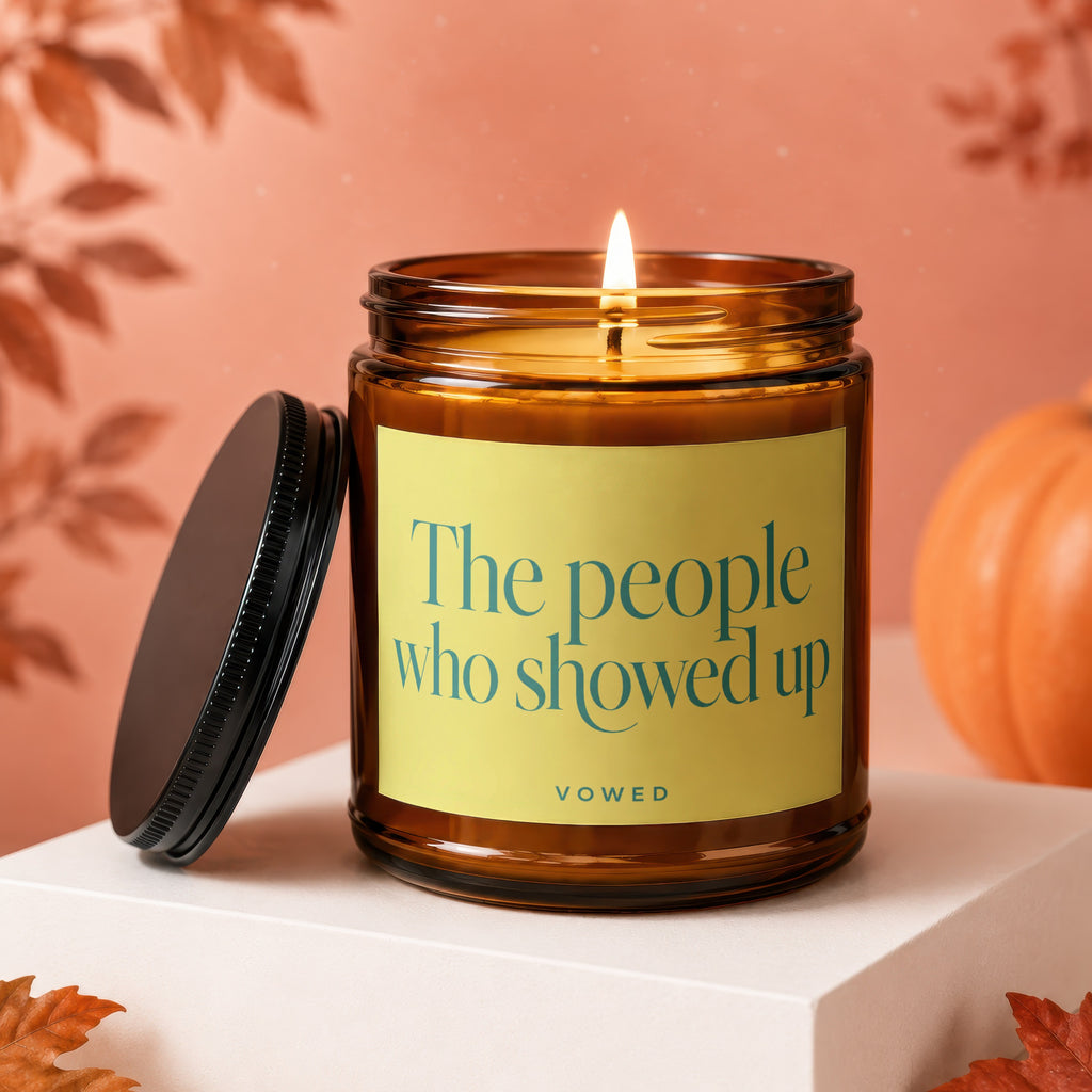 Amber jar candle with lit wick and label reading "The people who showed up VOWED."