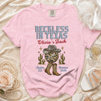 Pink t-shirt with "Reckless in Texas Olivia's Bach Austin, TX Summer 2026" text and cowboy boots.