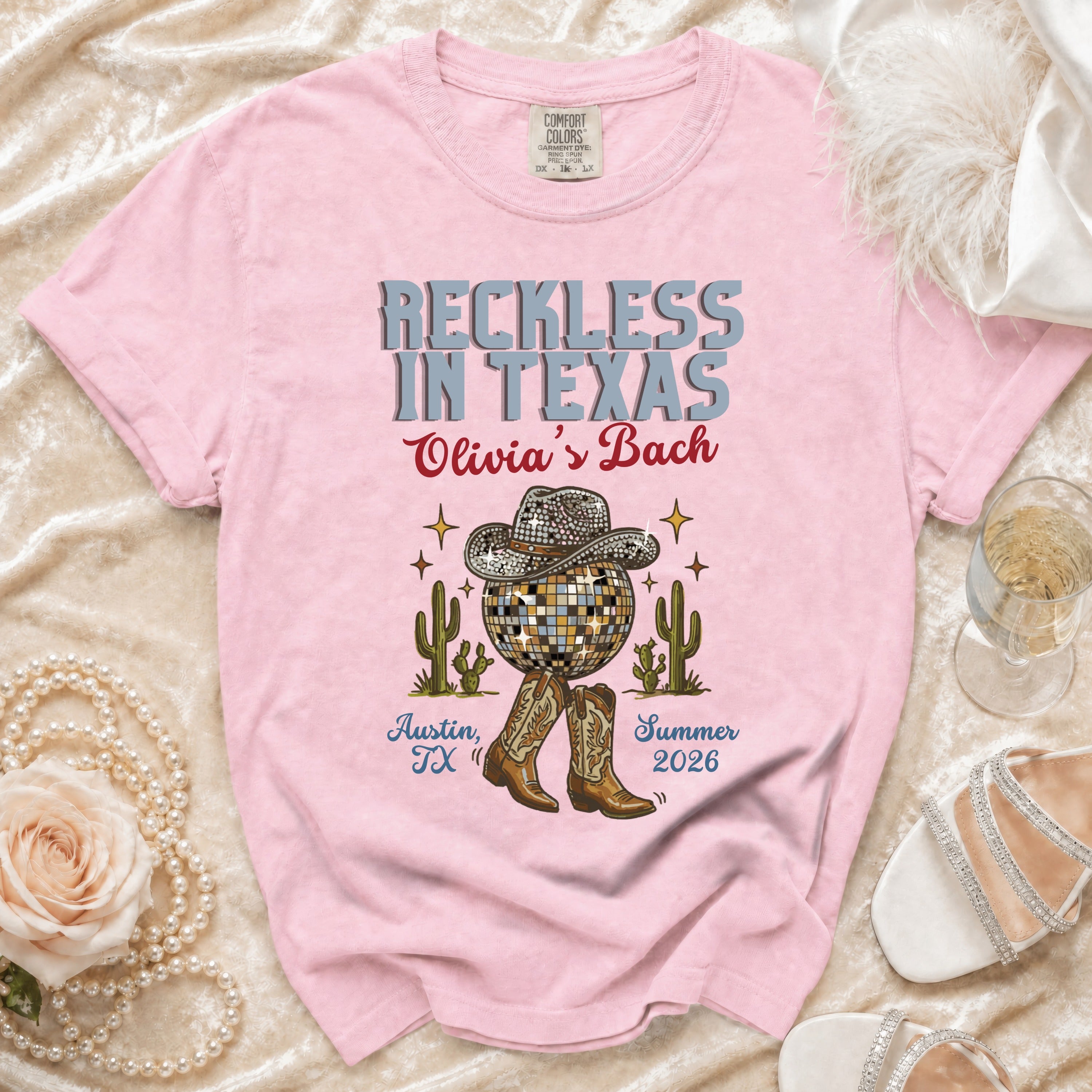 Pink t-shirt with "Reckless in Texas Olivia's Bach Austin, TX Summer 2026" text and cowboy boots.