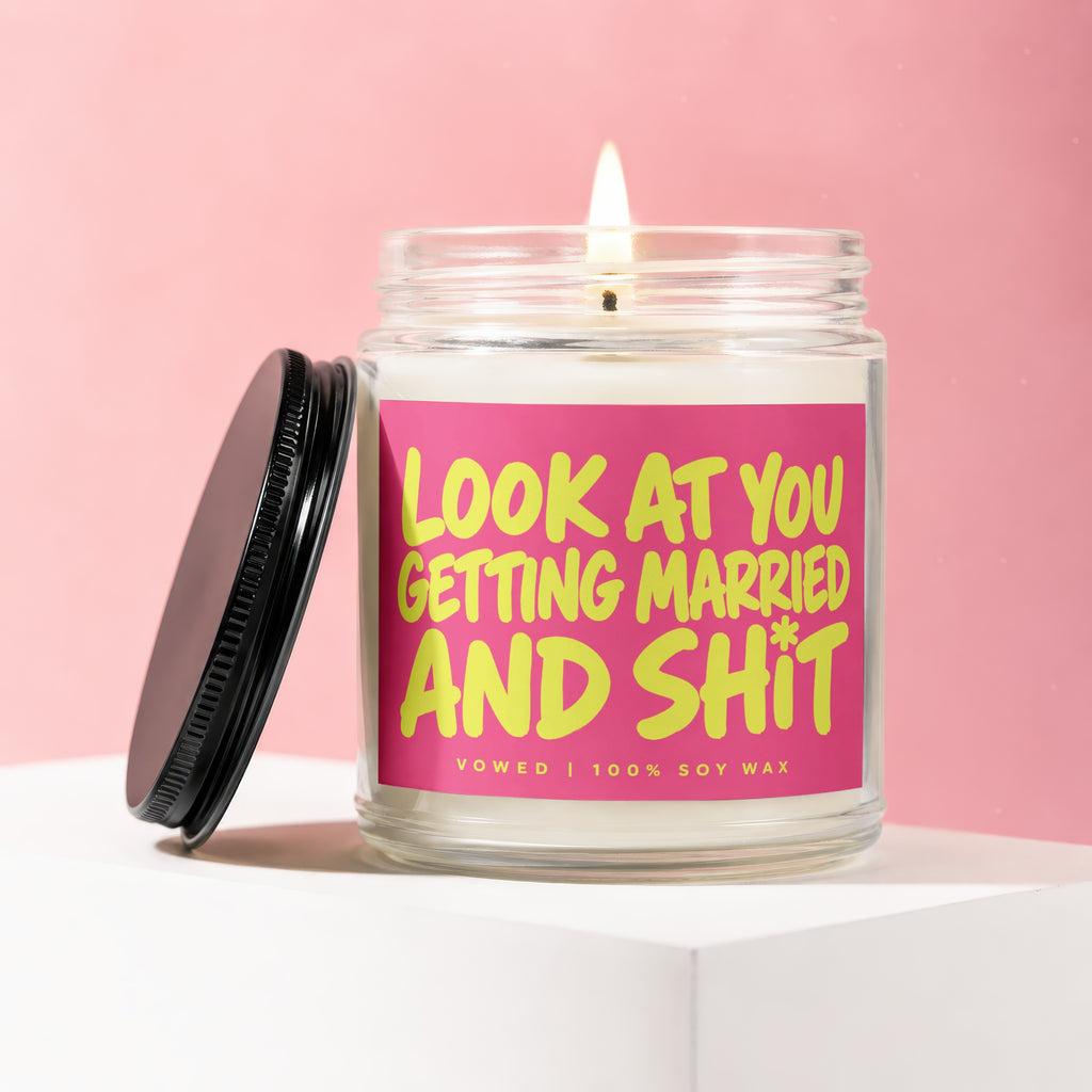 Lit candle in a glass jar with pink label reading "LOOK AT YOU GETTING MARRIED AND SHIT".