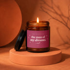 Amber candle with lit wick and pink label reading "the man of my dreams."