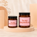 Two brown glass candles with pink labels reading "In my honeymoon era."